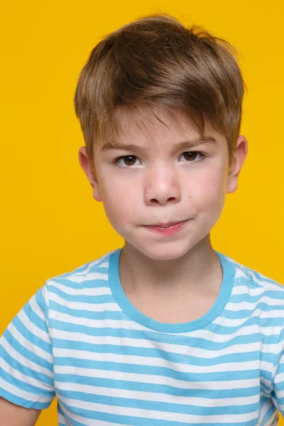 在明亮的橙色背景下 一个身穿白蓝色条纹衣服 表情不悦的可爱小男孩的画像 — 图库照片