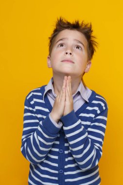 Çizgili süveter giyen komik bir çocuk ellerini yüzüne doğru kıvırdı ve parlak sarı bir arka planda izole edilmiş bir dua hareketi yaptı..