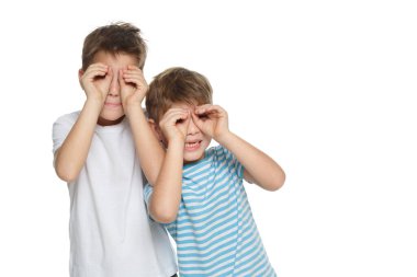 İki küçük komik çocuk beyaz bir arka planda izole edilmiş dürbün tasvir ederken ellerini yüzüne koydu..