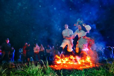 Bolshaya Rechka, Rusya - 25 Haziran 2017: Angara Nehri yakınlarındaki Beyaz Rusya tatili Ivan Kupala'yı kutlayan topluluk Krivichi, geceleri ateşin üzerinden atlayan ulusal elbiseler giymiş bir çift