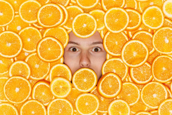 La cara del joven en el fondo de las naranjas jugosas en rodajas — Foto de Stock