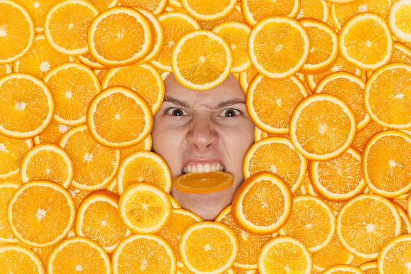Cara de hombre joven en rodajas jugosas naranjas mordiendo un pedazo de fruta con la cara enojada — Foto de Stock