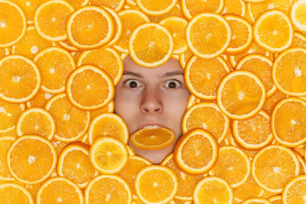 Face of young man on sliced juicy oranges biting a piece of fruit — Stock Photo, Image