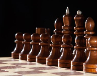 Siyah ahşap parçalı satranç tahtası karanlık arka planlı oyuna hazır.