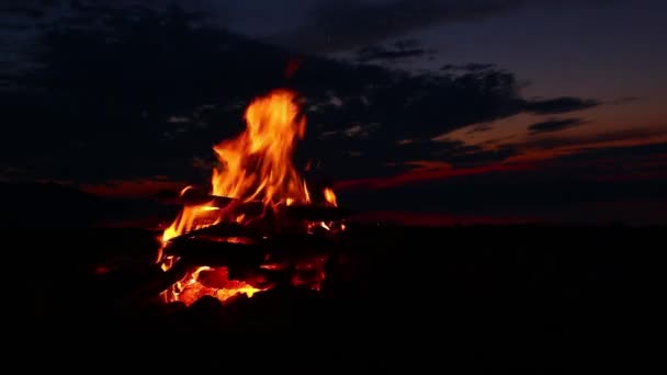 Fuego de campamento después del atardecer con cielo naranja y nubes oscuras en el fondo — Vídeos de Stock