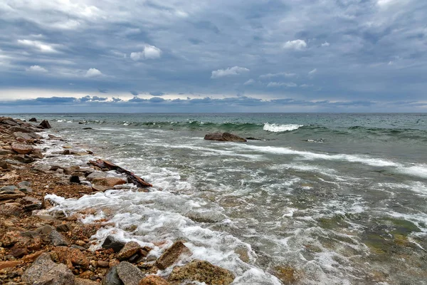 Stormy waves of Baikal lake in Russia with dark blue clouds and pebbles on the shore