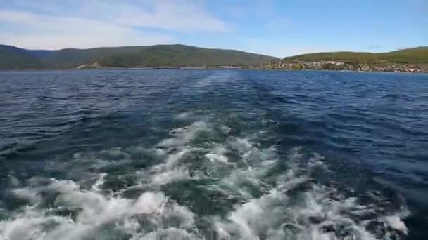 L'eau derrière grand bateau à moteur au lac Baikal avec le rivage vert un loin — Video
