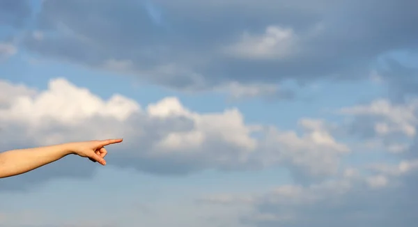 Hand pointing from left to right over blue sky and clouds background