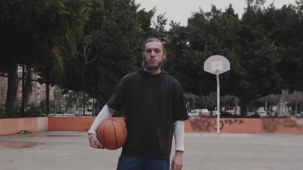 Jeune joueur de basket souriant tient la balle dans ses mains et regarde à la caméra — Video