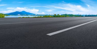 Boş asfalt yol meydanı ve mavi çizgilerin altında doğal manzara.