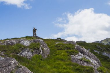 İskoçya, mavi gökyüzü ve büyük taşlar, yeşil çimen, fotoğraf makinesi ile modern büyük adam. Hobi, seyahat, Europe