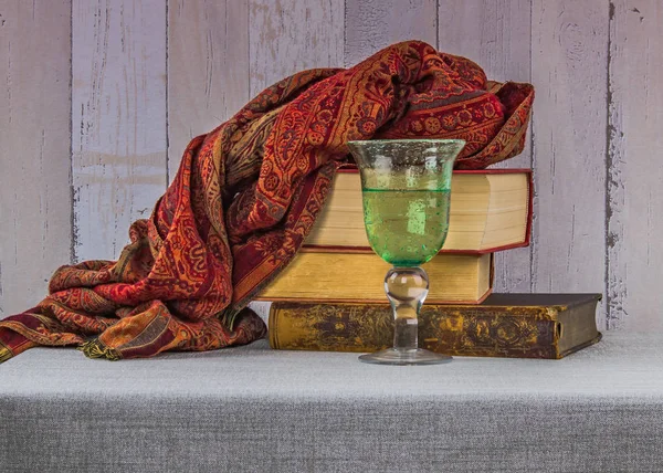 Still life with old books, a glass of drinking water and a luxurious cashmere shawl on the rustice background