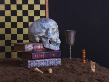 Cadılar Bayramı natürmort kafatası, satranç, satranç tahtası, kitap ve karanlık bir arka plan üzerinde şarap kadehi ile.