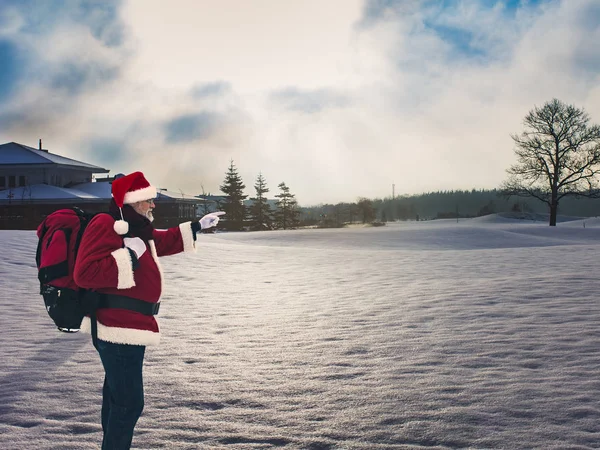 Karla kaplı sahada ayakta ve uzak ufuk parmak ile işaret sırt çantası ile sportif Noel Baba. Etkin sağlıklı yaşam tarzı ve Turizm kavramı.