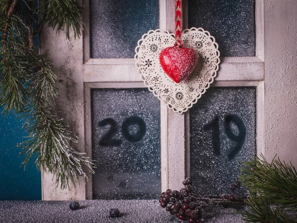Noel yılbaşı dekorasyonu - 2019 çizilmiş el ile karla kaplı penceresinin çerçeve, yazlık iç vurdu çam dalları, koni ve iki dekoratif kalp, kırmızı meyveler.