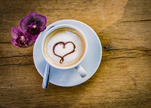 Cup of coffee with a heart and orchids (Phalaenopsis) on a wooden light brown table with copy space. valentine day with love, concept.
