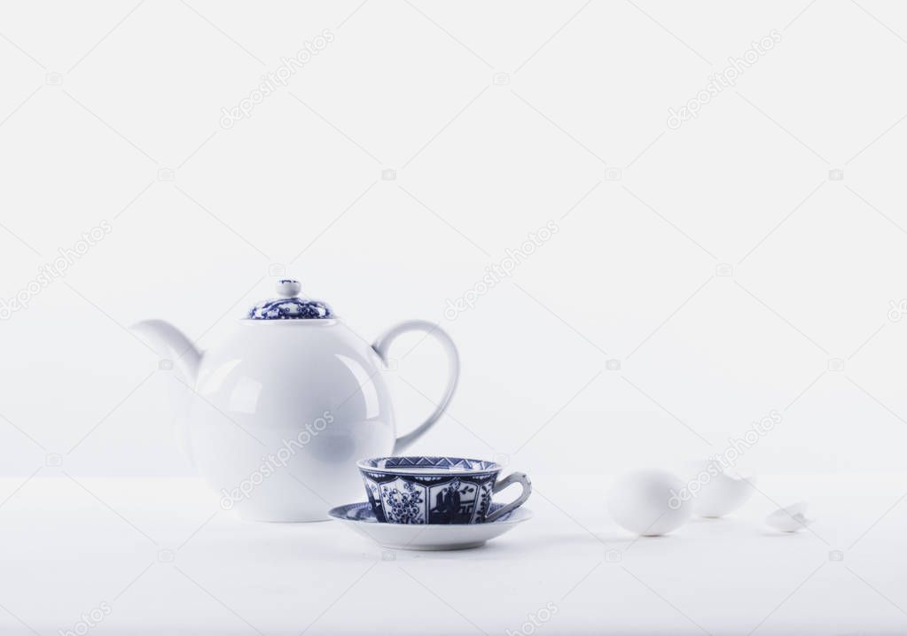 White still life with white teapot, white eggs on a white background and traditional cup of tea with china blue ornament