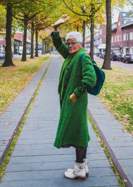 Şehir sonbahar sokakta yürüyen yeşil paltolu bir kıdemli dostu kadın portresi