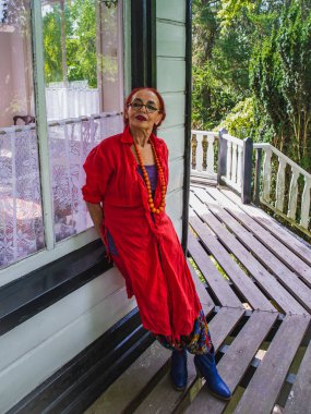 Balkonda poz kırmızı elbiseli modern şık yaşlı kadın o