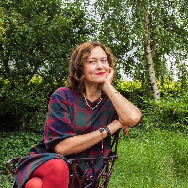 Приваблива усміхнена жінка середнього віку сидить у літньому парку — стокове фото