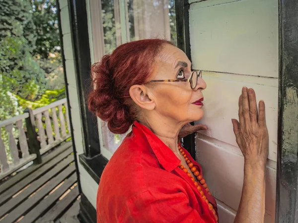 Uma mulher oriental idosa em um vestido vermelho visitou a casa velha  - — Fotografia de Stock