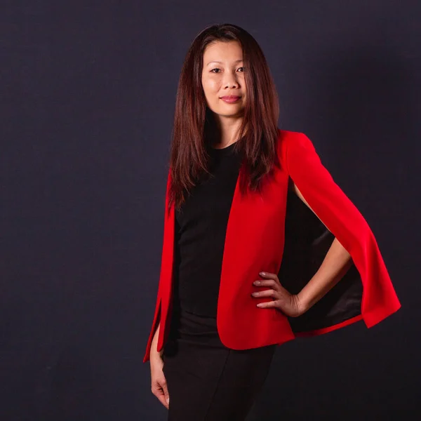 Belle brune asiatique en veste rouge debout sur un backgr sombre — Photo
