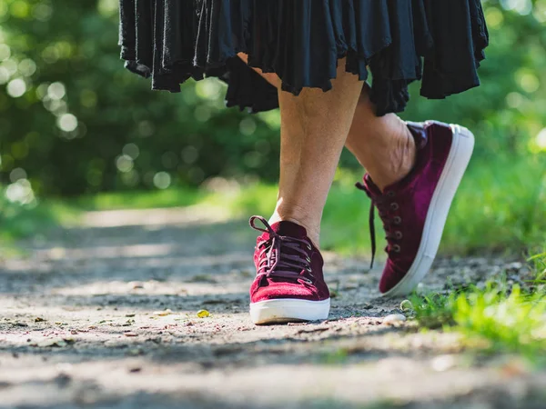 A woman wears stylish velvet shoes in maroon. Walking along a pa — Stock Photo, Image