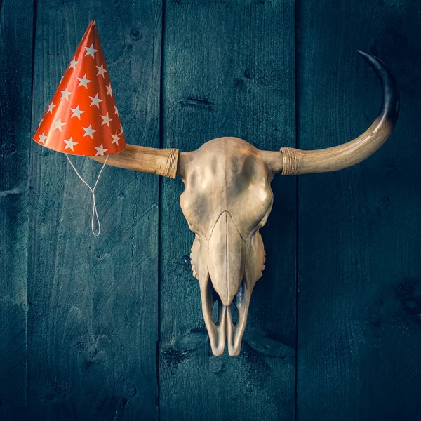 Buffalo skull with hanging paper red hat with stars on long horns. Country style, wooden rough texture background with space for text.