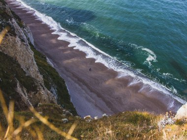 Okyanus dalgalarıyla dolu çapraz su çizgisinden muhteşem bir manzara. Fransa 'nın Normandiya kıyıları boyunca yürüyen birkaç insan.