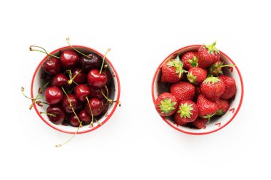 Beyaz arka planda izole edilmiş çilek ve kirazlı iki kırmızı kase..