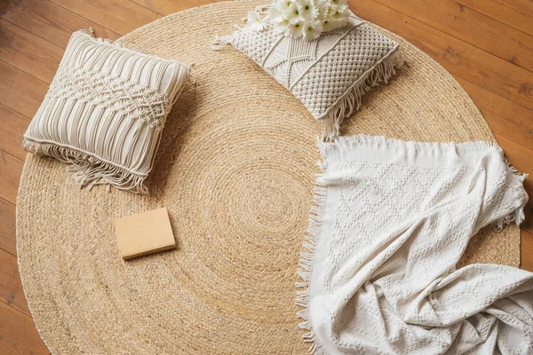 A cozy place to read on the floor. Jute woven round carpet, macrame pillows, plaid and book.