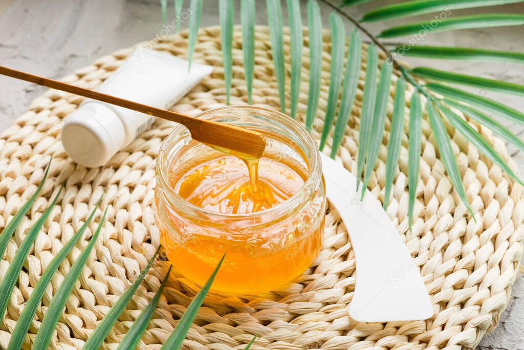 Sugar paste to remove hair on a wooden stick. Sugaring paste in a glass jar on wicker bedding. An alternative to waxing.