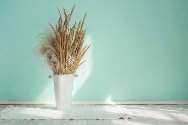 Beyaz demir vazo kovası. Mavi bir duvarın arka planında otlardan yapılmış kuru kulakları var. Kopya alanı ile boho biçiminde iç ayrıntılar.