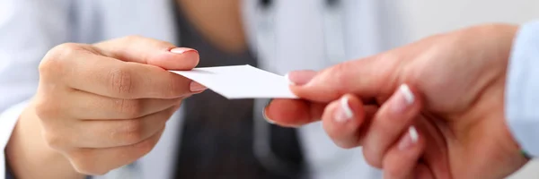 Female physician hand give white blank calling card to businesswoman closeup in office. Physical, disease prevention, examine patient, instrument shop, healthy lifestyle, family doctor concept