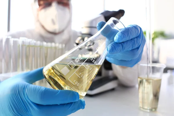 Brazo científico en guantes protectores sostiene líquido amarillo en botella —  Fotos de Stock