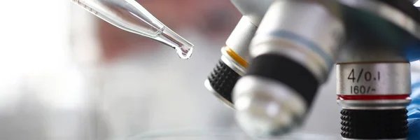Científico dosificando una gota con pipet para examinarla con microscopio — Foto de Stock