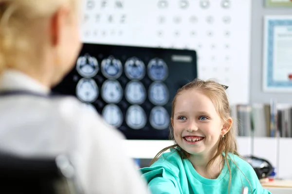 Leende söt liten flicka som pratar med kvinnlig läkare på hennes kontor — Stockfoto