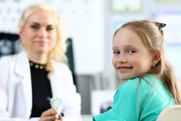 Söt leende liten flicka porträtt med kvinnlig läkare i bakgrunden — Stockfoto