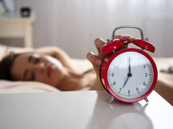 Female hand turning off disturbing noisy alert from red alarm clock