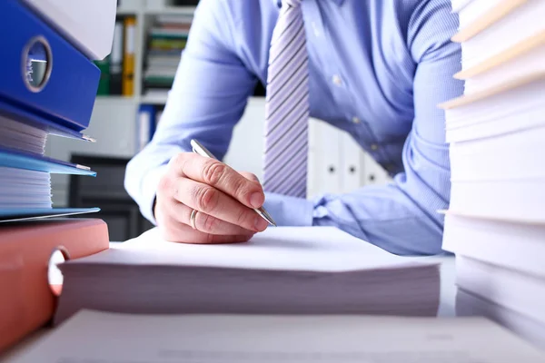 Male hand holding silver pen working with huge pack of paper documents Royalty Free Stock Images