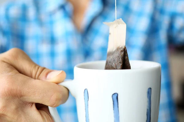 Man in blue shirt making cup of tea using modern handy teabag