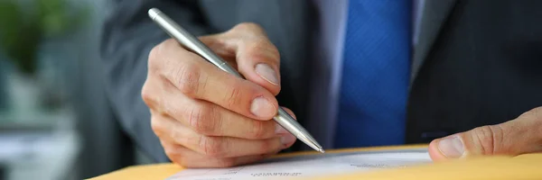 Männlicher Angestellter in Anzug und Krawatte am Arbeitsplatz hält silbernen Stift in den Händen und füllt Bewerbungsformular aus — Stockfoto