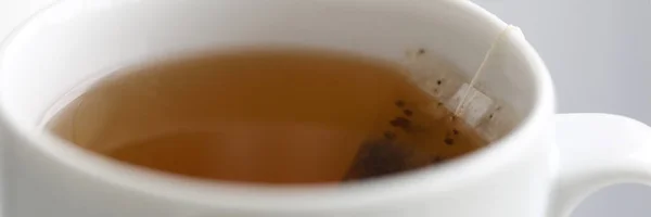 Teabag fresco fabricado em copo branco pendurado fora da borda — Fotografia de Stock