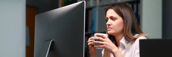 Mujer sostiene taza y mira el monitor intensamente — Foto de Stock
