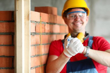 Miğferli inşaatçı tuğla işçiliğinin yanında durur ve gülümser.