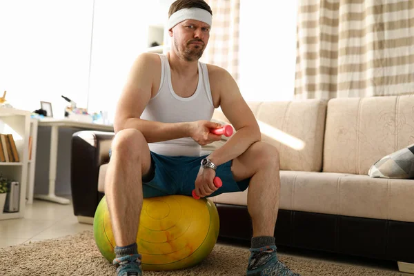 Чоловік вдома сидить на м'ячі в руках гантелі — стокове фото