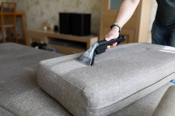 Male housekeeper hand cleaning sofa with washing suction cleaner
