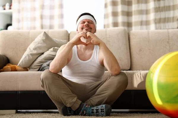 Guy senta-se em casa tapete medita e mostra o coração — Fotografia de Stock