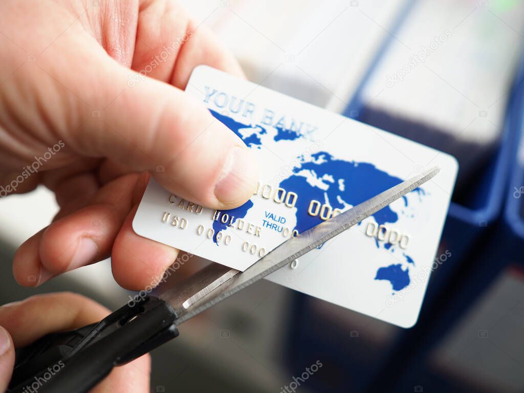 Male hand cutting banking card with scissors