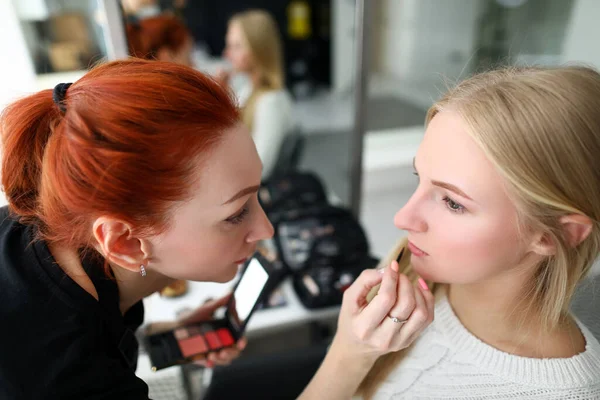 Makeup artist holds cosmetic brush near face model